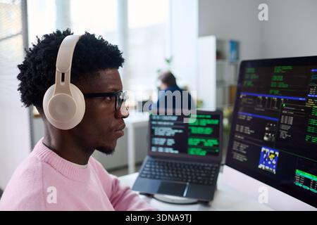 Young Black Man Wearing Headphones Working on Computer Programming Code Stock Photo