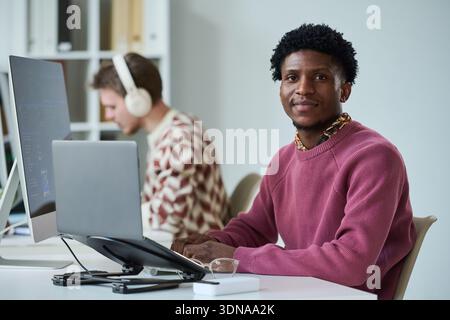 Portrait of Young Black Man Smiling While Sitting at Office Desk Stock Photo