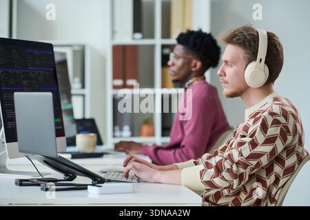 Young Man Wearing Headphones Working on Computer Beside Black Man Stock Photo