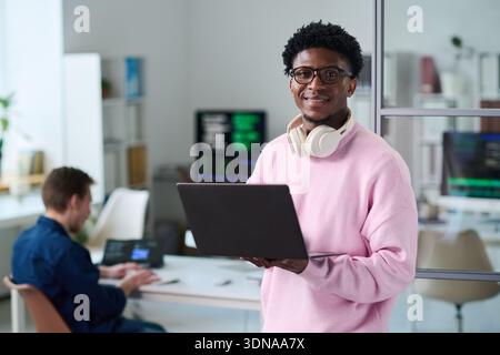 Portrait of Young Black Man Holding Laptop and Smiling in Office Stock Photo