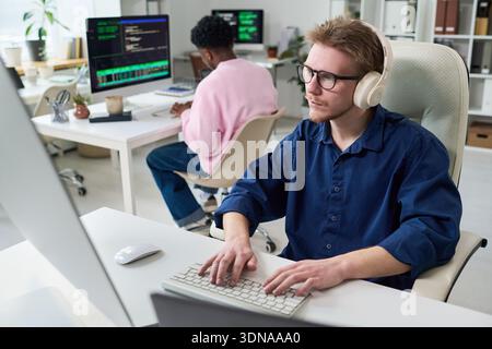 Young Man Wearing Headphones Typing on Keyboard in Office Stock Photo