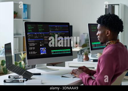Young Black Man Analyzing Programming Code on Desktop Computer Screen Stock Photo