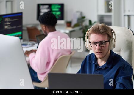 Young Man Wearing Headphones Working on Computer in Office Stock Photo