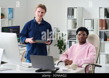 Portrait of Young Man Standing Beside Young Black Man Working Stock Photo