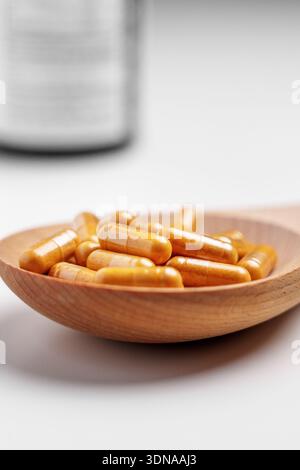 Golden herbal capsules placed in a wooden spoon. Dietary supplement on white table with pills bottle on background Stock Photo