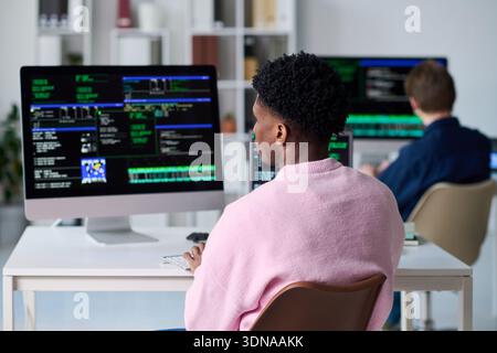 Young Black Man Writing Code on Computer in Office Setting Stock Photo
