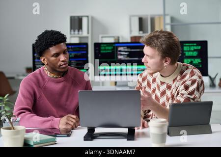 Young Man Explaining Project to Young Black Man in Office Setting Stock Photo