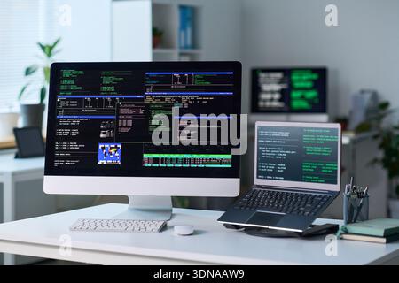 Office Desk Featuring Computer and Laptop Displaying Programming Code Stock Photo