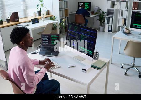 Young Black Man Coding on Computer in Office with Multiple Monitors Stock Photo