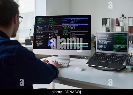 Young Man Coding Software Applications on Desktop and Laptop Stock Photo