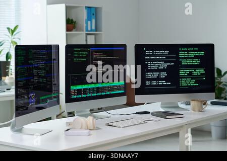 Three Computer Monitors Displaying Programming Code in Office Setting Stock Photo