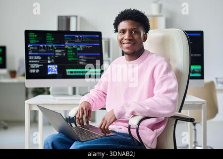 Portrait of Young Black Man Smiling While Working on Laptop in Office Stock Photo