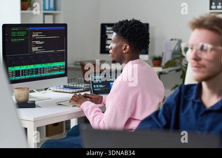Young Black Man Debugging Software Code on Desktop Computer in Office Stock Photo