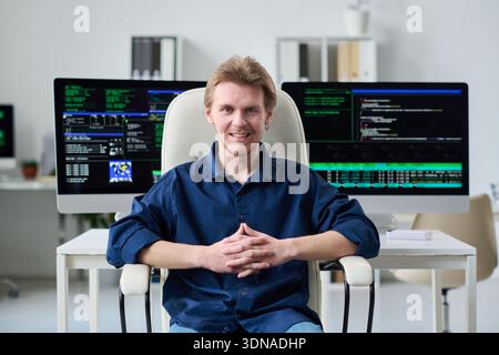 Portrait of Young Man Smiling While Sitting in Front of Computers Stock Photo