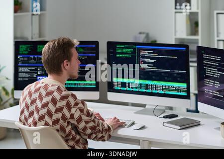 Young Man Working with Code on Multiple Computer Monitors Stock Photo