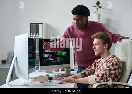Young Black Man Explaining Programming Code to Young Man Stock Photo