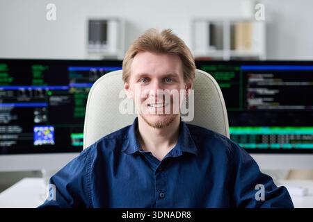 Portrait of Young Man Smiling While Sitting in Front of Monitors Stock Photo