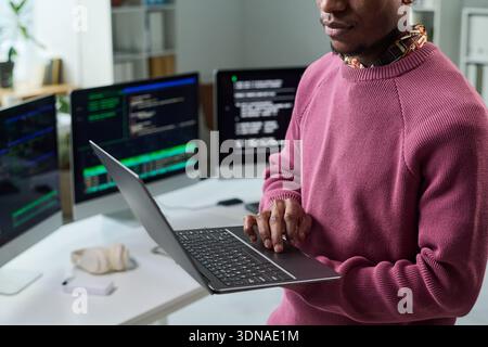 Young Black Man Reviewing Software Code on Laptop in Technology Office Stock Photo