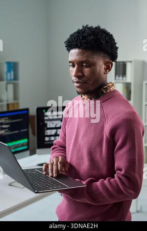 Young Black Man Using Laptop While Standing in Office Workspace Stock Photo