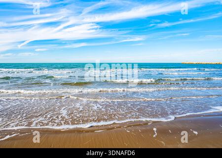 Clear Adriatic waves rolling onto the sandy shore under wispy clouds, Apulia, Italy Stock Photo