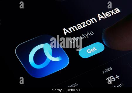Amazon Alexa app download screen on Apple iPad with redesigned Alexa logo, dark mode App Store listing, and finger tapping Get button highlighting Ale Stock Photo