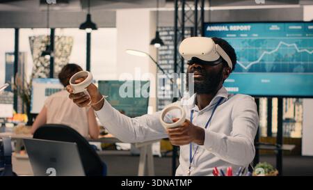 African American man wearing VR headset goggles in a modern office, interacting with computer-generated images and 3D simulation. Virtual reality and artificial intelligence for business analytics. Stock Photo