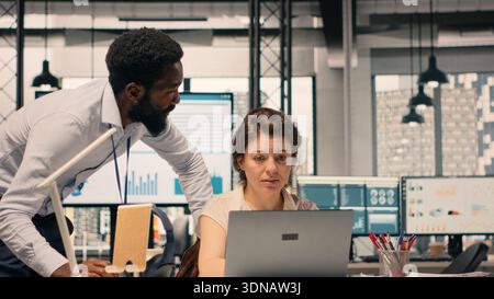 Diverse work team in a multinational company office discussing forecasting and resource allocation. Visual data and reports displayed on laptop support strategic planning and goals achievement. Stock Photo