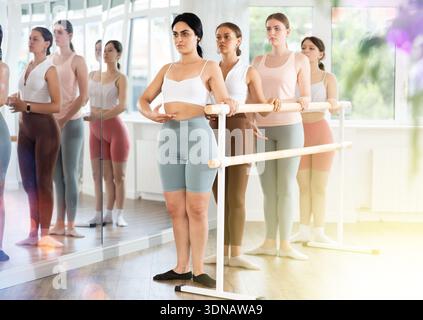 Young ballerinas stand in second position near ballet barre during group training in dance studio Stock Photo