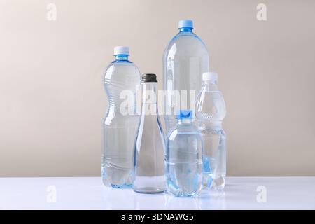 Water bottles of different sizes on white table against beige background Stock Photo