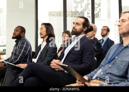 Diverse people in audience listening to guest speaker during business forum with panel discussion, international conference event. Professionals and listeners attend leadership convention. Stock Photo