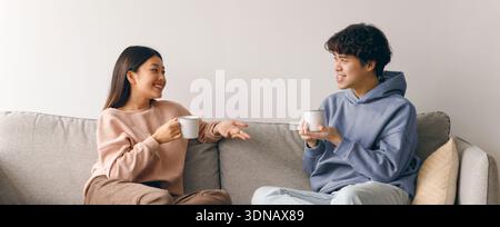 Young Couple Enjoys Conversation Over Coffee on a Comfortable Sofa During the Afternoon Stock Photo