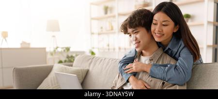 Young Couple Enjoys Time Together at Home While Looking at a Laptop on the Couch Stock Photo