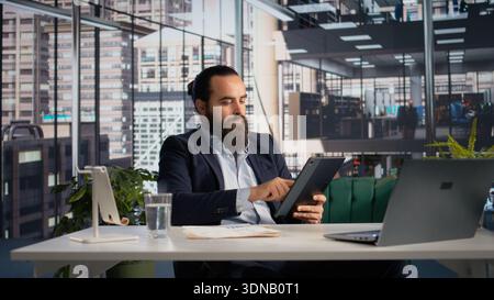 Business leader fact-checking documents with company data and KPIs on tablet, reviewing performance metrics in order to create a new strategy. Business management with decision making. Stock Photo