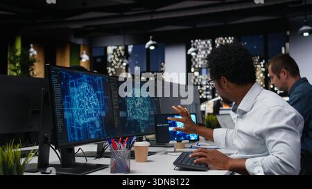 Tech startup IT professional developing AI algorithms in high rise office during late night shift. African american man debugging neural network brain models on screens Stock Photo