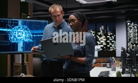 Engineering team in office analyzing machine learning algorithms using tablet and laptop. Coworkers discussing, using devices to improve artificial intelligence prediction accuracy Stock Photo