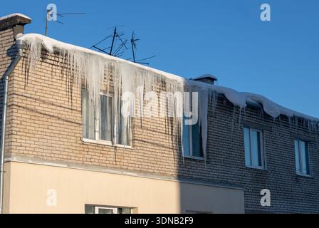 Giant icicles hanging down from the roof of an old residential brick house. Dangerous icicles hangs from the roof. Harsh nord winter. Stock Photo