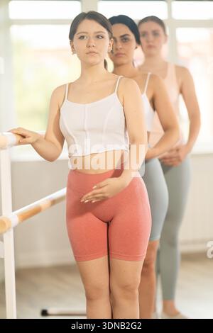 Young ballerinas stand in second position near ballet barre during group training in dance studio Stock Photo