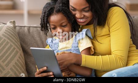 Mother and Daughter Share Moments While Using a Tablet Together on a Couch Stock Photo