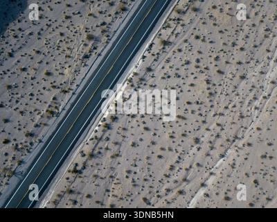 Aerial drone view looking straight down on a sparse Mojave desert with a two lane asphalt road crossing the frame diagonally Stock Photo