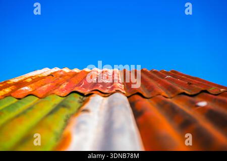Old and rusted corrugated tin roof panels sloping upward towards a clear blue sky. Stock Photo