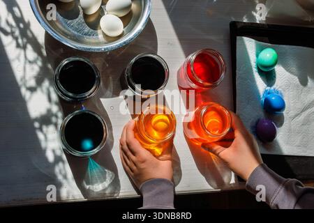 Top view of the hands arranging dye jars for easter egg coloring on sunlit table. Stock Photo