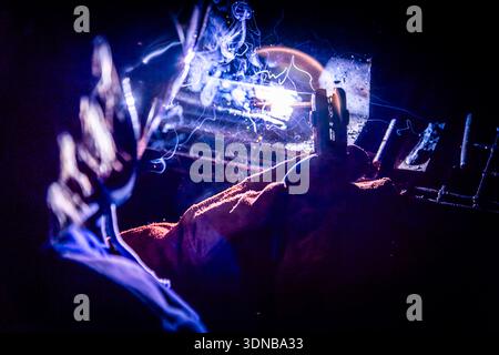 Close-up of a female welder welding metal with intense sparks and arc light, hands in protective gloves, industrial workshop. Stock Photo