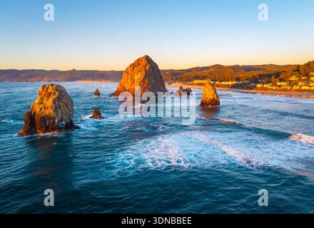 A breathtaking aerial view of Haystack Rock and the Cannon Beach coastline, bathed in the warm, golden light of a vibrant sunset over the Pacific Ocea Stock Photo