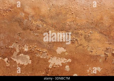weathered plaster wall surface, peeling orange paint with damp stains and bubbling masonry texture, closeup view, grunge background and urban decay Stock Photo