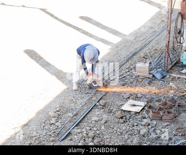 A high-angle view of a construction worker using a metal chop saw to cut steel rebar on a construction site with bright sparks flying across the groun Stock Photo