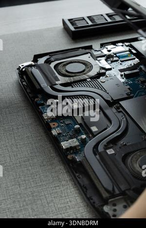 A laptop is opened on a flat surface, showing its internal parts like circuit boards and fans. Tools sit nearby, suggesting ongoing repair work. Stock Photo
