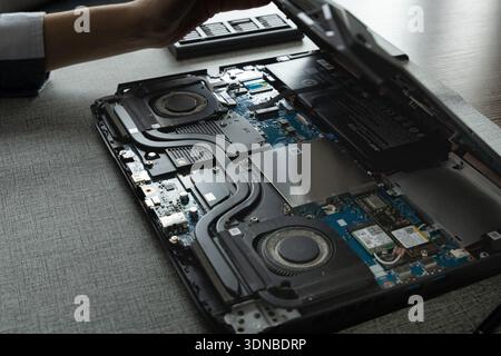 A person is opening a laptop to repair it. The workspace is neat and organized, with soft lighting coming in. Stock Photo