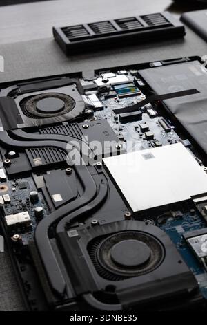 A laptop is opened and parts are shown on a work surface. The internal components include fans, circuit boards, and wires. Stock Photo