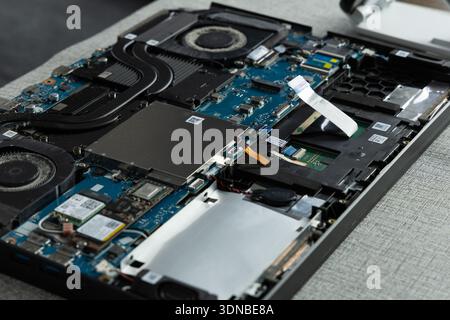 A laptop is open on a gray table, showing its internal parts. The repair person is working on replacing or fixing components inside the device. Stock Photo