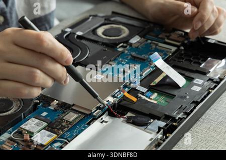 Hands are working on the inside of a laptop, using a tool to fix components on a blue circuit board. Stock Photo